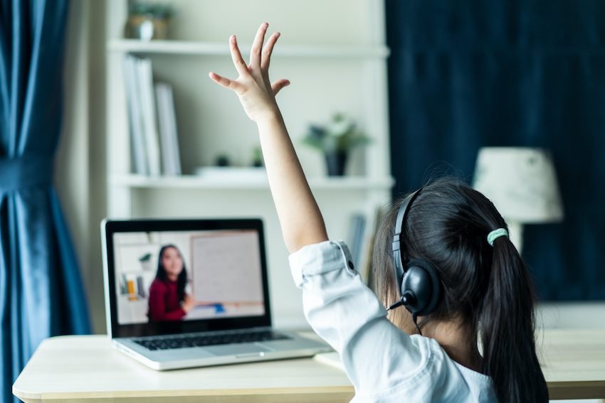 Homeschool Asian little young girl student learning virtual internet online class from school teacher by remote meeting due to covid pandemic. Female teaching math by using headphone and whiteboard.