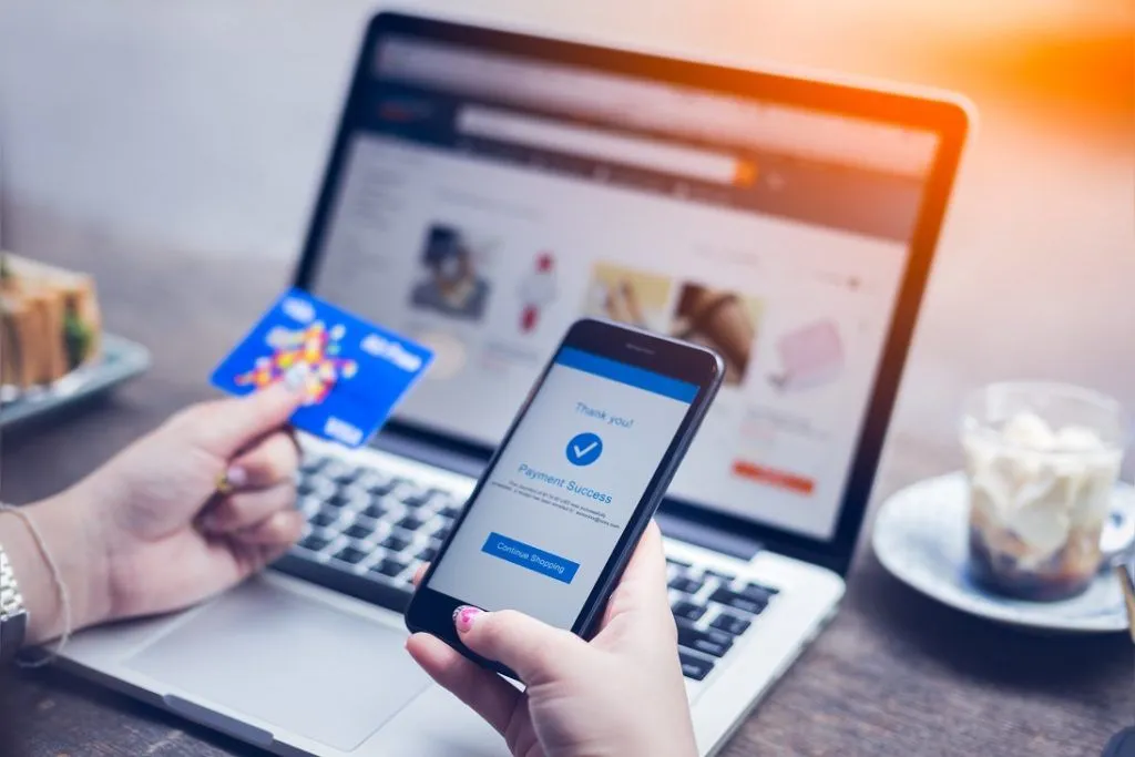 A woman is using an online payment gateway while holding a credit card and a laptop.